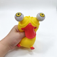 A yellow rubber frog toy with protruding eyeballs and a red tongue, being held by a hand against a plain white background.