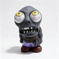 A stylized zombie figurine with oversized white eyes, yellow sclera, a dark gray body, brown shoes, and a purple garment, photographed on a clean white studio background.