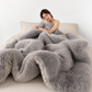 Woman wrapped in a fluffy gray blanket on a bed with a white background