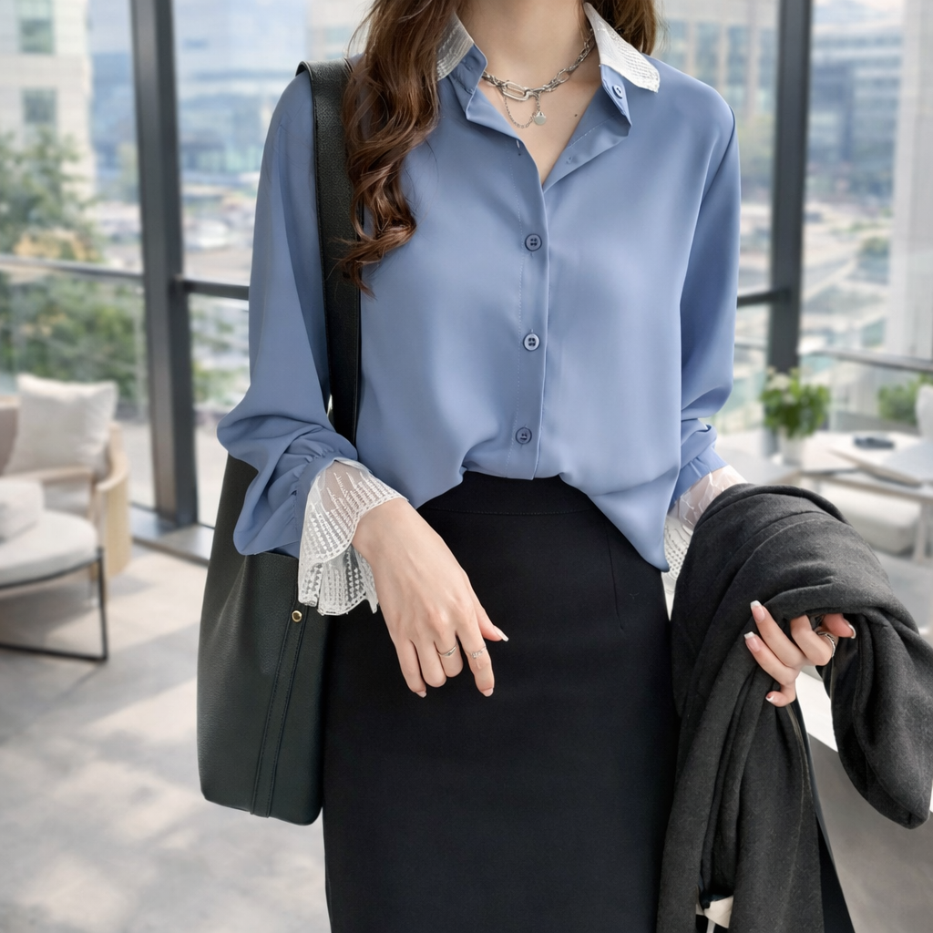 Woman in a blue shirt and black skirt holding a black bag and jacket in an indoor setting with large windows.