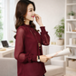 Woman in a burgundy blouse holding a newspaper in a home setting