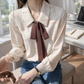 Woman wearing a beige blouse with a brown tie and blue jeans in an office setting.