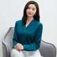 Woman wearing a green teal blouse sitting on a gray chair against a white background
