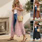 Woman wearing a long pink floral dress with blue jeans and brown sandals, holding a straw bag.