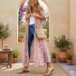 Woman wearing a long pink lace dress standing in a sunlit outdoor setting with plants and a table.
