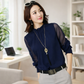 Woman wearing a navy blue blouse with sheer sleeves in a bright room.