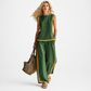 Woman wearing a green outfit with yellow accents, holding a woven bag on a white background