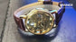 Gold mechanical watch with brown leather strap on a white background
